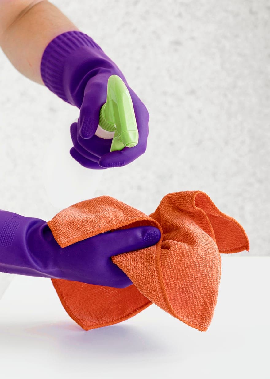 Purple-gloved hands spraying cleaner onto a cloth for a home clean